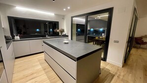 Una cocina moderna con una isla grande, un comedor con mesa y sillas, y vista al salón a través de un vidrio.