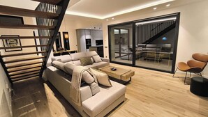 Una sala de estar moderna con un sofá modular grande, una mesa de centro y una escalera que sube a un nivel superior.