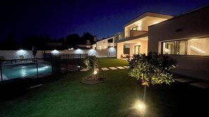 Una casa moderna con piscina, zona exterior bien iluminada y un pequeño jardín.