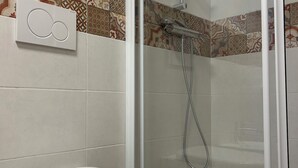 A bathroom with a toilet, a shower with a glass door, and patterned tiles on the walls. - Camera famigliare un letto matrimoniale e 1 lettini (Corropoli)