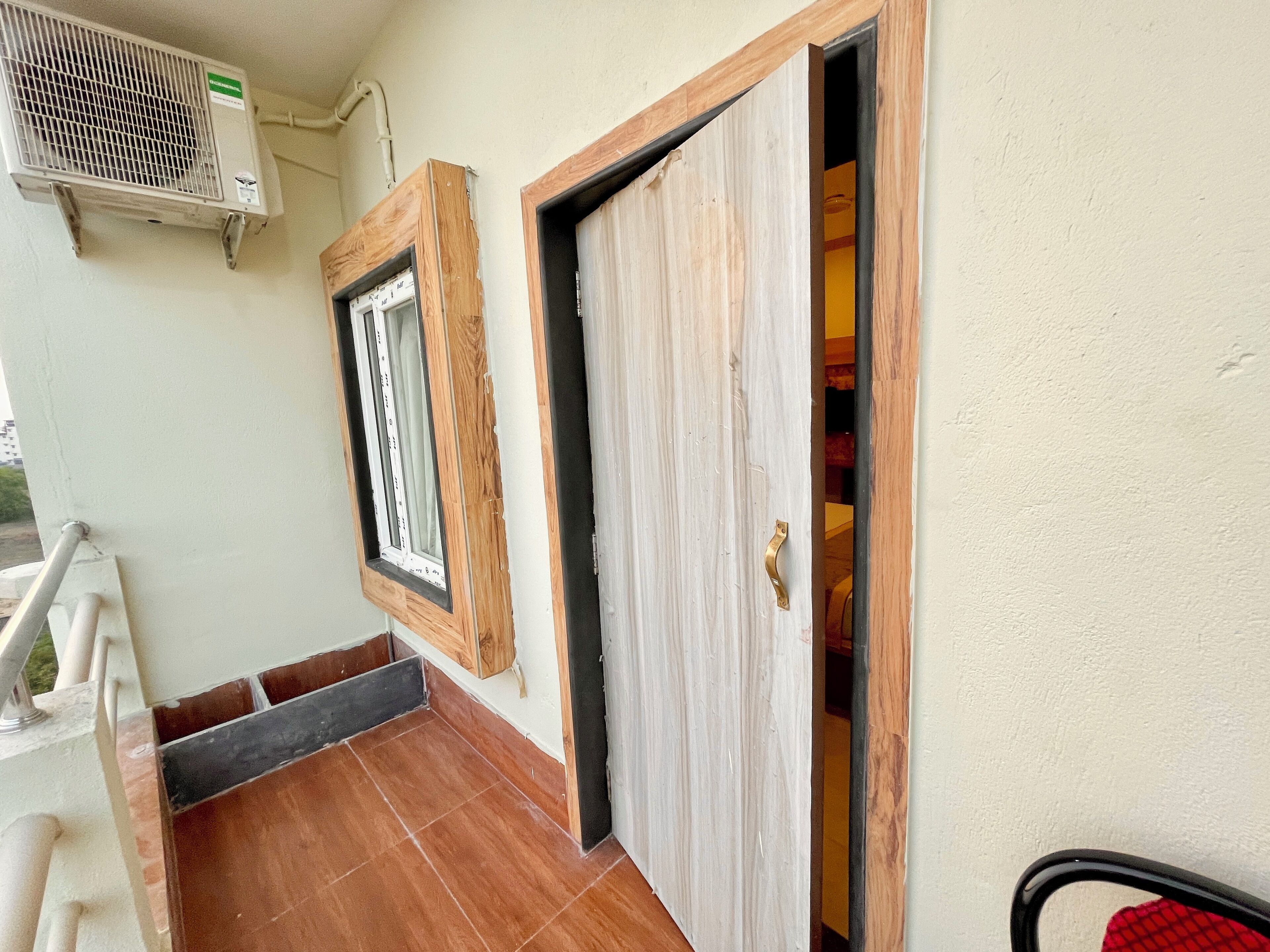 Una habitación con una puerta de madera, una ventana con marco de madera y una unidad de aire acondicionado blanca instalada en la pared.