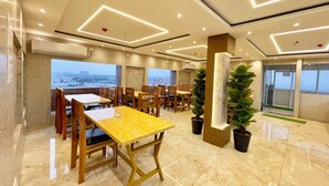 A modern dining area with marble flooring, wooden tables and chairs, and large windows offering a city view.