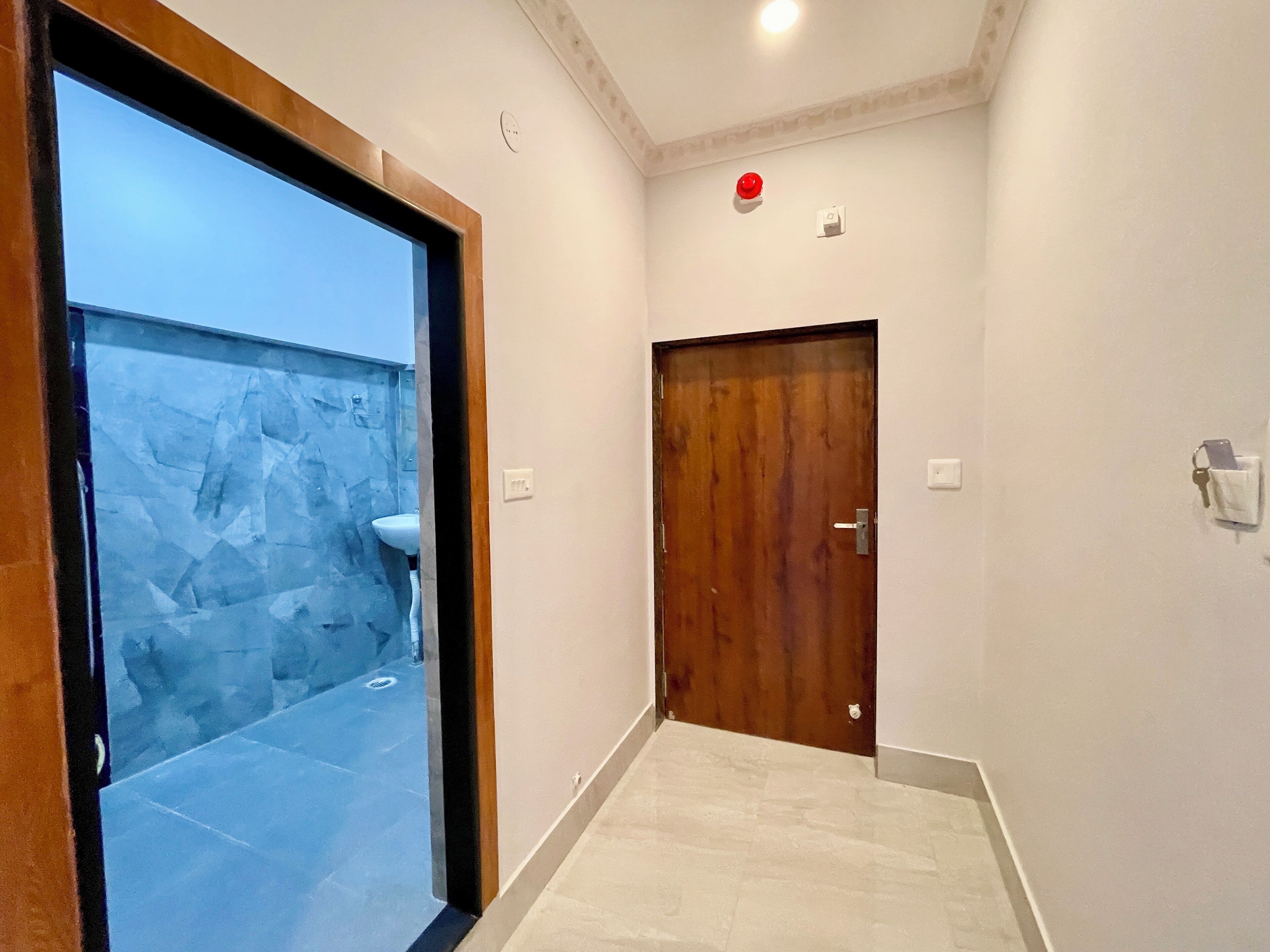 A hallway with a wooden door, a white wall, and a stone wall with a sink.