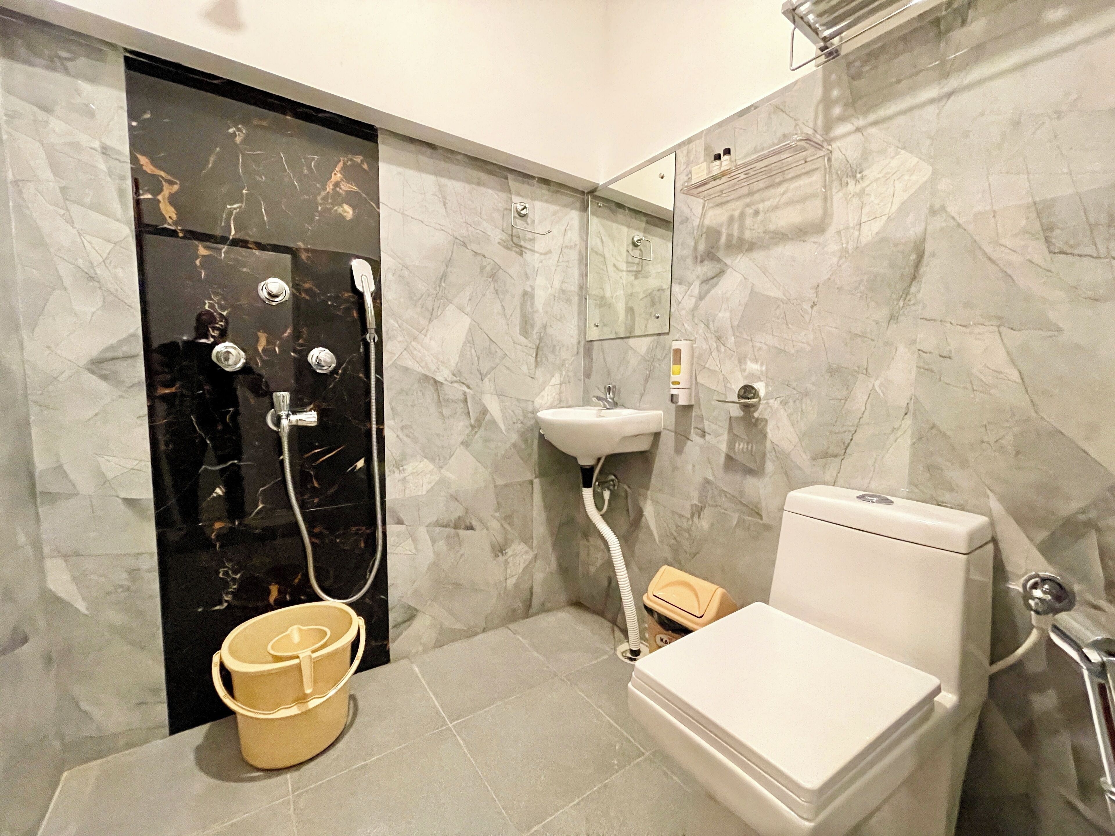 A bathroom with a black marble shower enclosure, a white sink, a toilet, and a beige bucket.