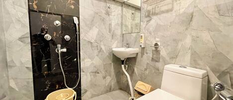 A bathroom with a black marble shower enclosure, a white sink, a toilet, and a beige bucket.