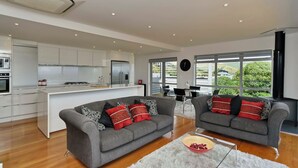 Eine moderne Küche mit weißen Schränken, einer zentralen Kochinsel und einem Essbereich mit zwei grauen Sofas und einem Couchtisch.