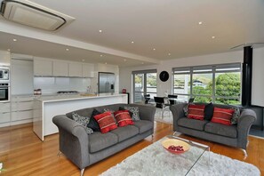 Uma cozinha moderna com armários brancos, uma ilha central e um espaço de refeições com dois sofás cinzas e uma mesa de centro.