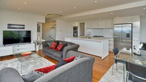 Ein modernes Wohnzimmer mit einem grauen Sofa, einem Glastisch und einem Flachbildfernseher.