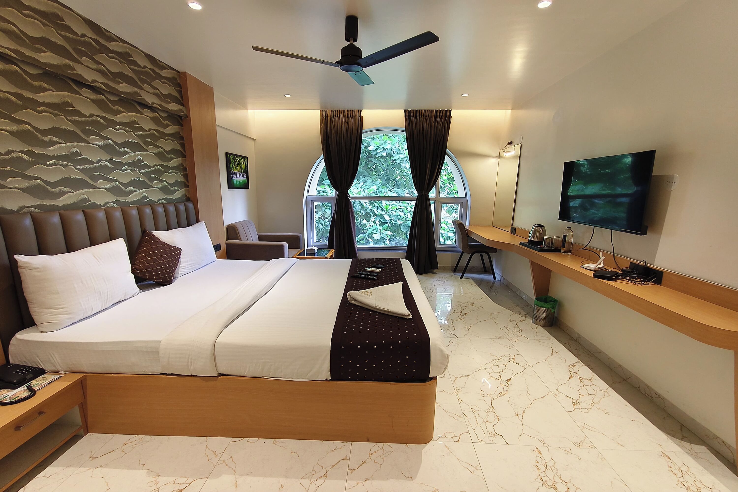 A modern hotel room with a large bed, a desk, a TV, and a ceiling fan.