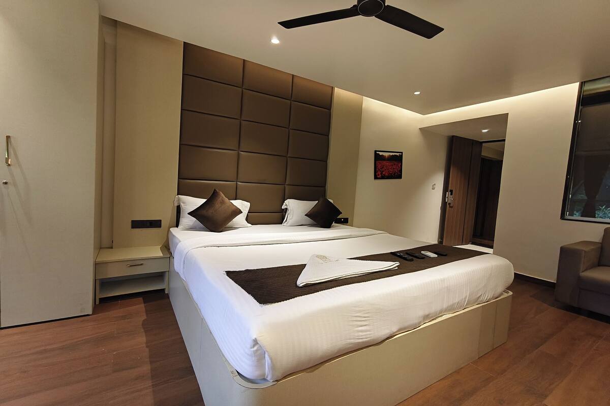 Quarto de hotel moderno com uma cama grande, um ventilador de teto, uma mesa de cabeceira e uma TV fixada na parede.