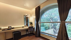 Ein modernes Zimmer mit einem großen Fenster, einem Schreibtisch mit Wasserkocher, einem Stuhl und einem kleinen schwarzen Gerät.