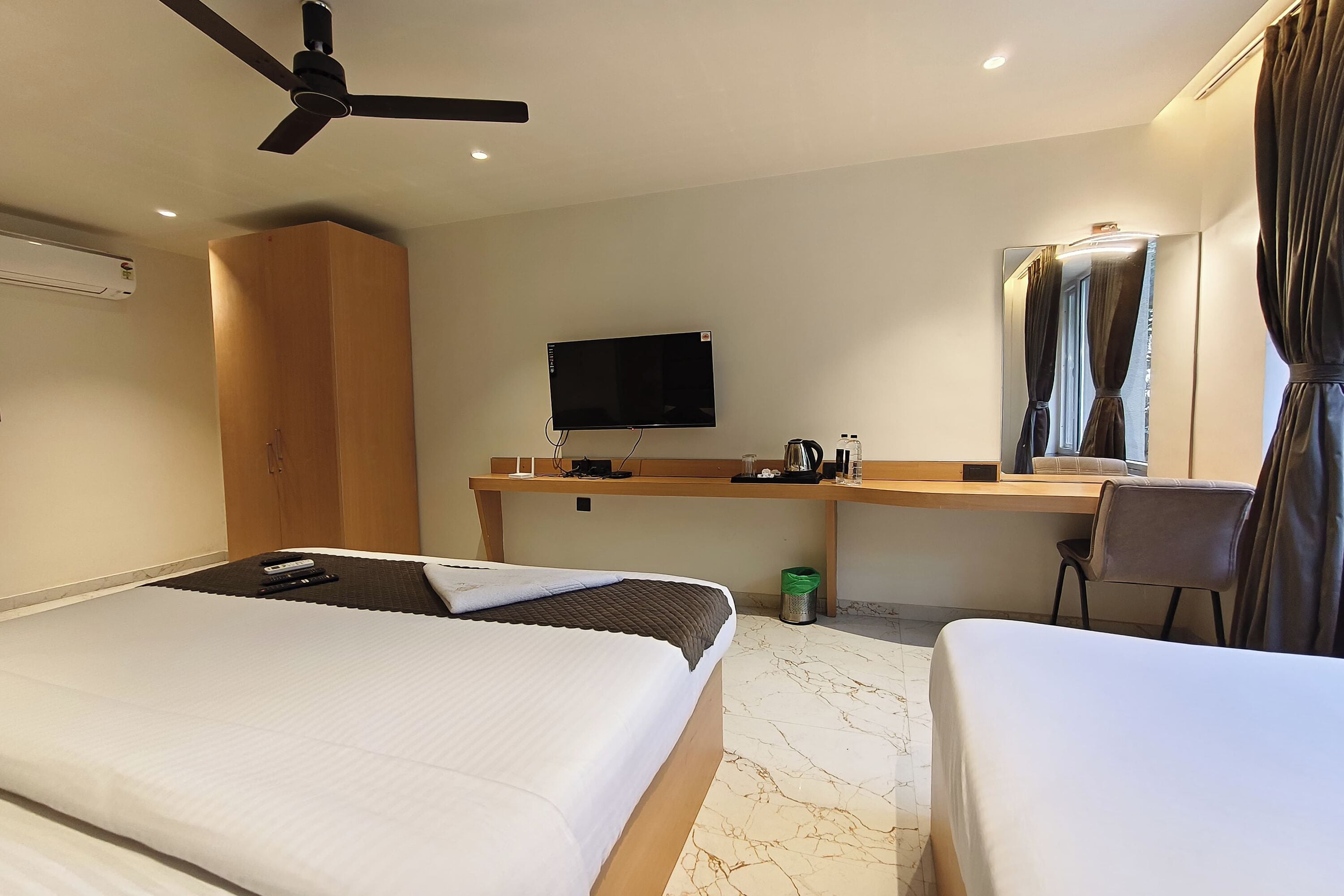 Une chambre d’hôtel avec deux lits, un bureau, une télévision et un ventilateur de plafond.