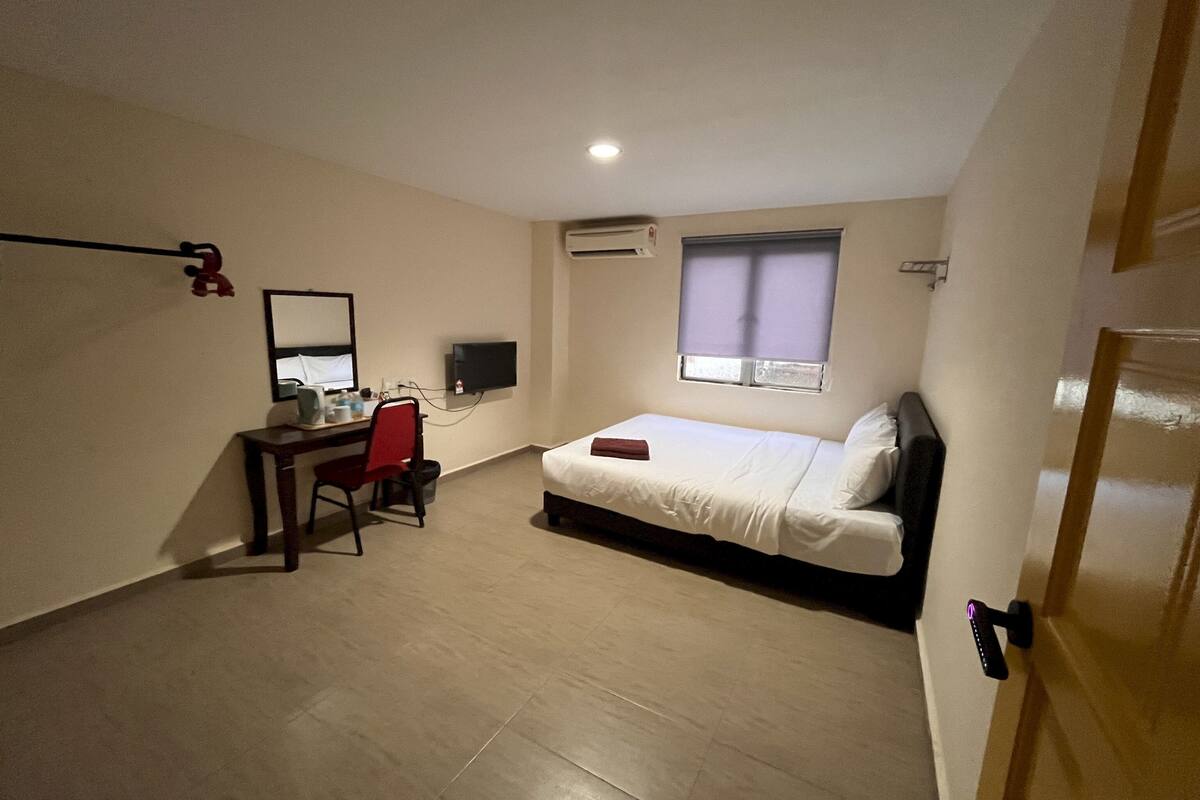 A bedroom with a bed, a desk, a chair, a mirror, and an air conditioning unit.