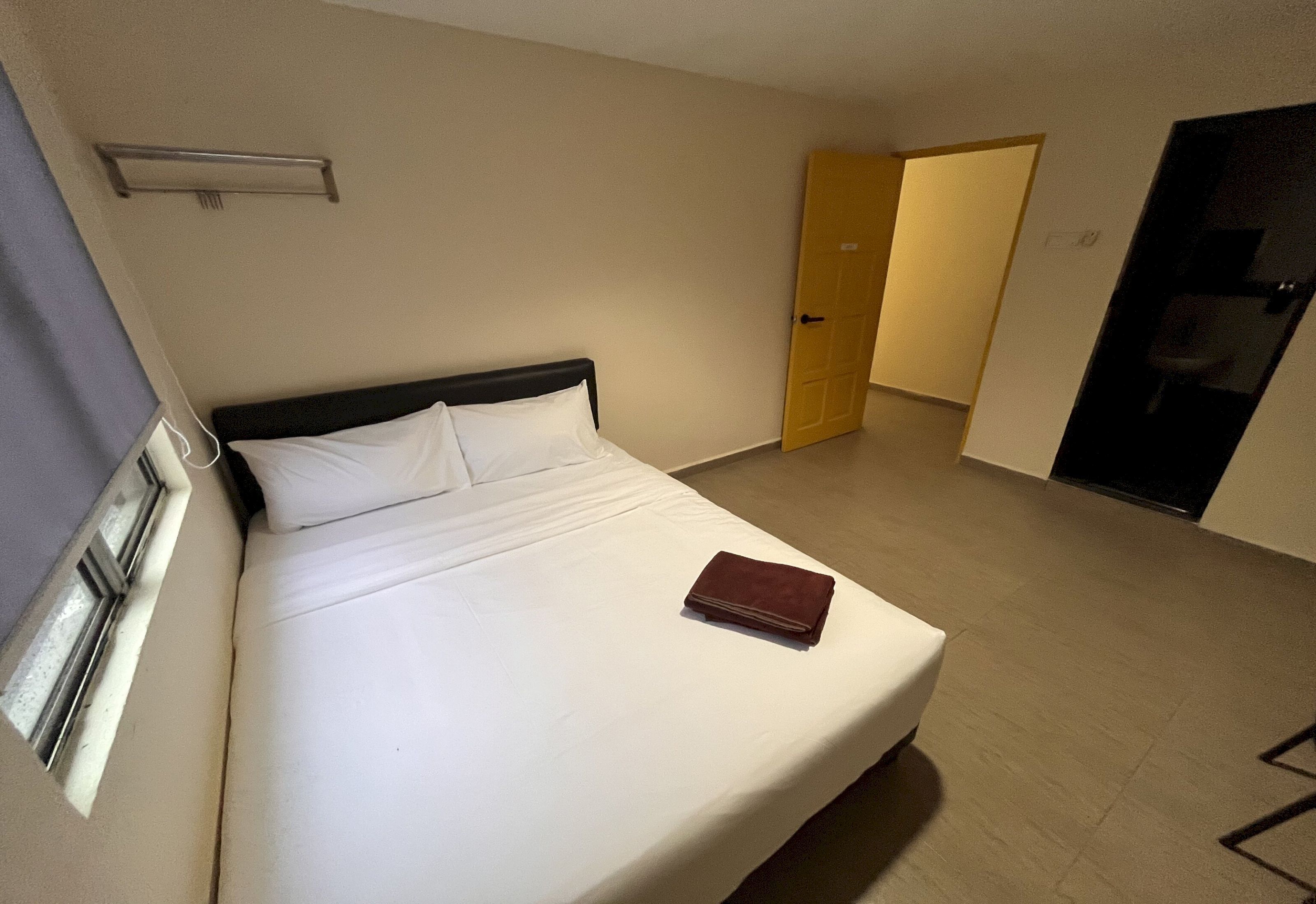 A hotel room with a bed, a bedside table, a door, and a window.