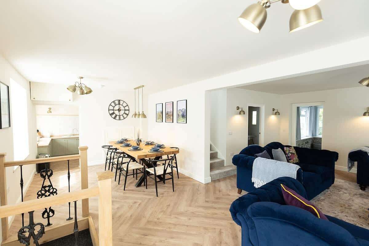 A modern living room with a blue sofa, a dining area with a wooden table, and a staircase leading to another level.