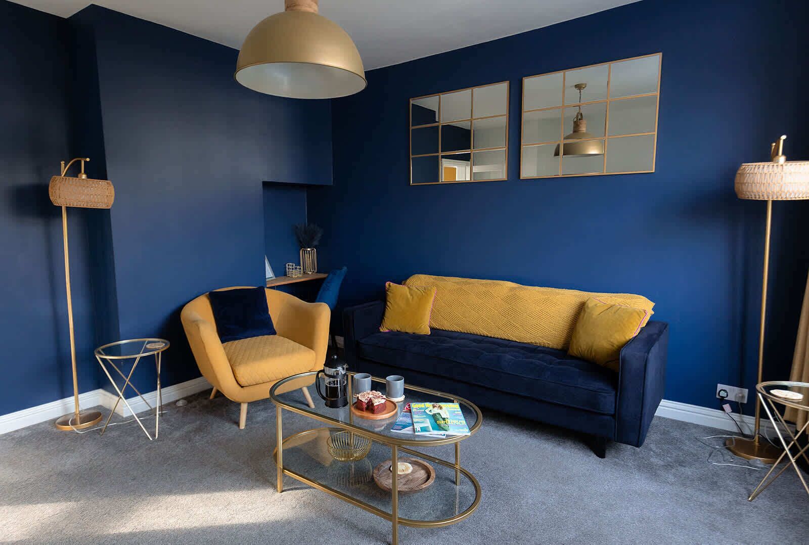 Un salon avec un canapé bleu, un fauteuil jaune, une table basse et deux lampadaires.