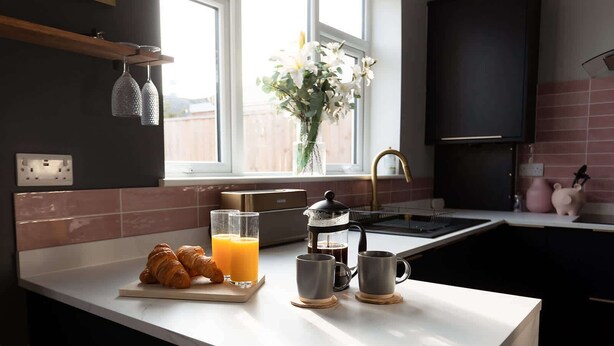 Eine Küche mit weißer Arbeitsplatte, einer Kaffeemaschine, zwei Gläser Orangensaft und Croissants.
