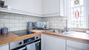 A modern kitchen with white cabinets, a wooden countertop, a built-in dishwasher, and a window with a stained glass design.