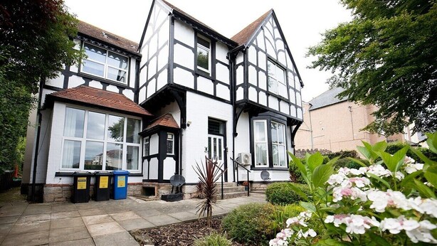 A traditional Tudor-style building with a symmetrical facade, large windows, and a well-maintained garden with flowering plants.