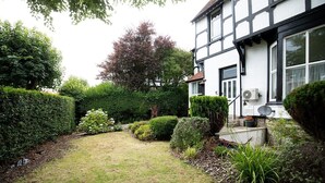 A traditional half-timbered house with a well-maintained garden, including hedges and a lawn.