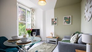 A modern living room with a glass dining table, grey sofa, and a television.