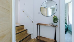 Una scala con gradini in legno e una ringhiera nera, che conduce a un pianerottolo con uno specchio rotondo e un piccolo ripiano con una pianta e oggetti decorativi.
