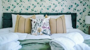 Un letto rifatto con un cuscino floreale, una testata verde e una parete decorata con un motivo a foglia.