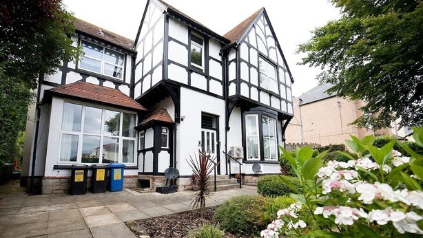 Una casa in stile Tudor tradizionale, con facciata simmetrica, ampie finestre e un giardino curato con piante fiorite.