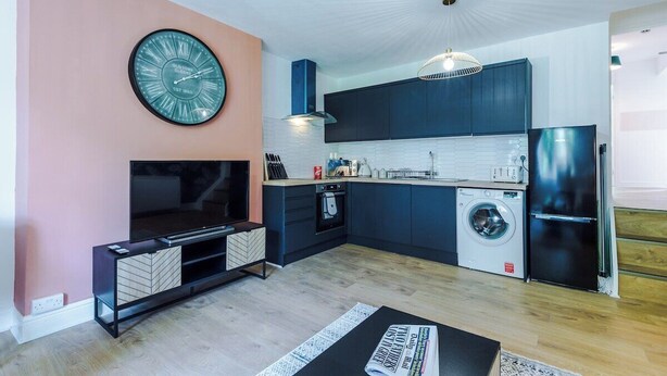 Una cucina moderna con lavatrice integrata, un orologio grande e un televisore a schermo piatto.