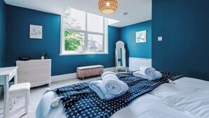 Una camera da letto con un'ampia finestra, un letto con asciugamani arrotolati, una cassettiera, uno specchio e una lampada a sospensione.