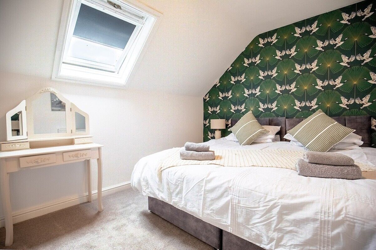 A bedroom with a bed, a bedside table, a mirror, and a window.