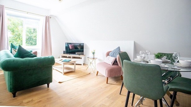 A modern living room with a green sofa, a pink armchair, and a dining table set for four. - The Anchorage Apartments - No.6 (Conwy Principal Area)
