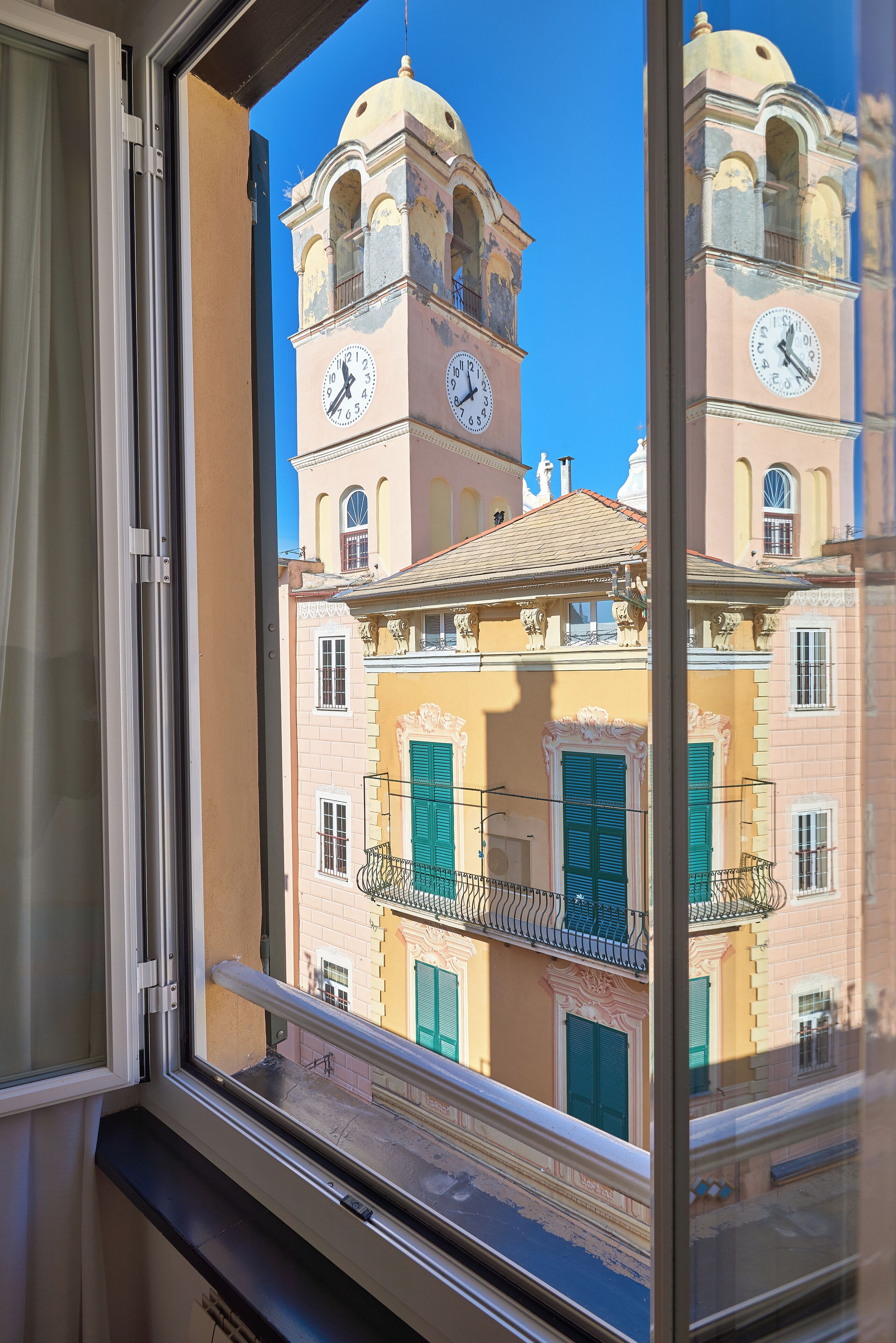 A view through a window of a building with a clock tower, balconies, and a clear blue sky.