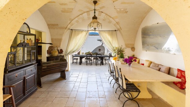 A dining area with a long table, chairs, and a bench. There is a chandelier above the table and a large painting on the wall. - 4015 Masseria Scilla by Barbarhouse (Carovigno)
