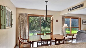 A dining area with a wooden table and chairs, a chandelier, and a view of the outdoors.