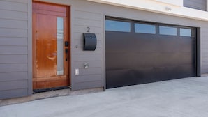 A modern garage with a large black door, a wooden front door, and a mailbox on the wall.
