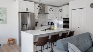 A modern kitchen with white cabinets, a stainless steel refrigerator, a built-in oven, and a central island with bar stools.