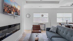 A modern living room with a flat-screen TV, a fireplace, a sofa, a coffee table, and a dining area with a table and chairs.