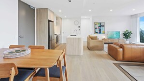 Una sala de estar moderna con sofá, una mesa de comedor con sillas, una zona de cocina y un ventanal grande.