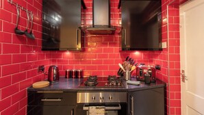 Une cuisine compacte aux murs recouverts de carreaux rouges, dotée d’appareils électroménagers en acier inoxydable et d’un plan de travail noir.