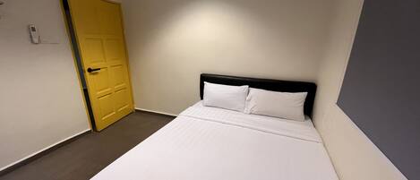 A single bed with white bedding in a room with a yellow door and light-colored walls.