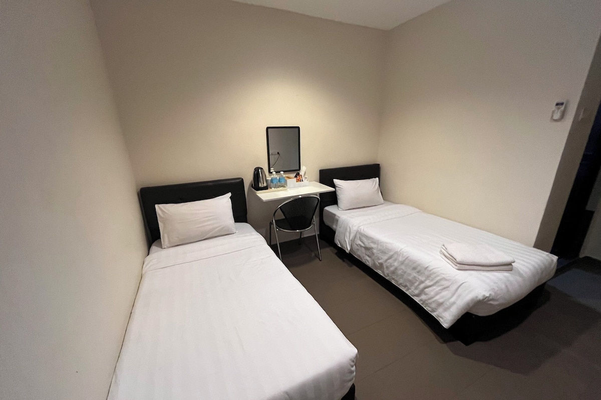 Una habitación de hotel pequeña con dos camas individuales, un escritorio con silla y un espejo.