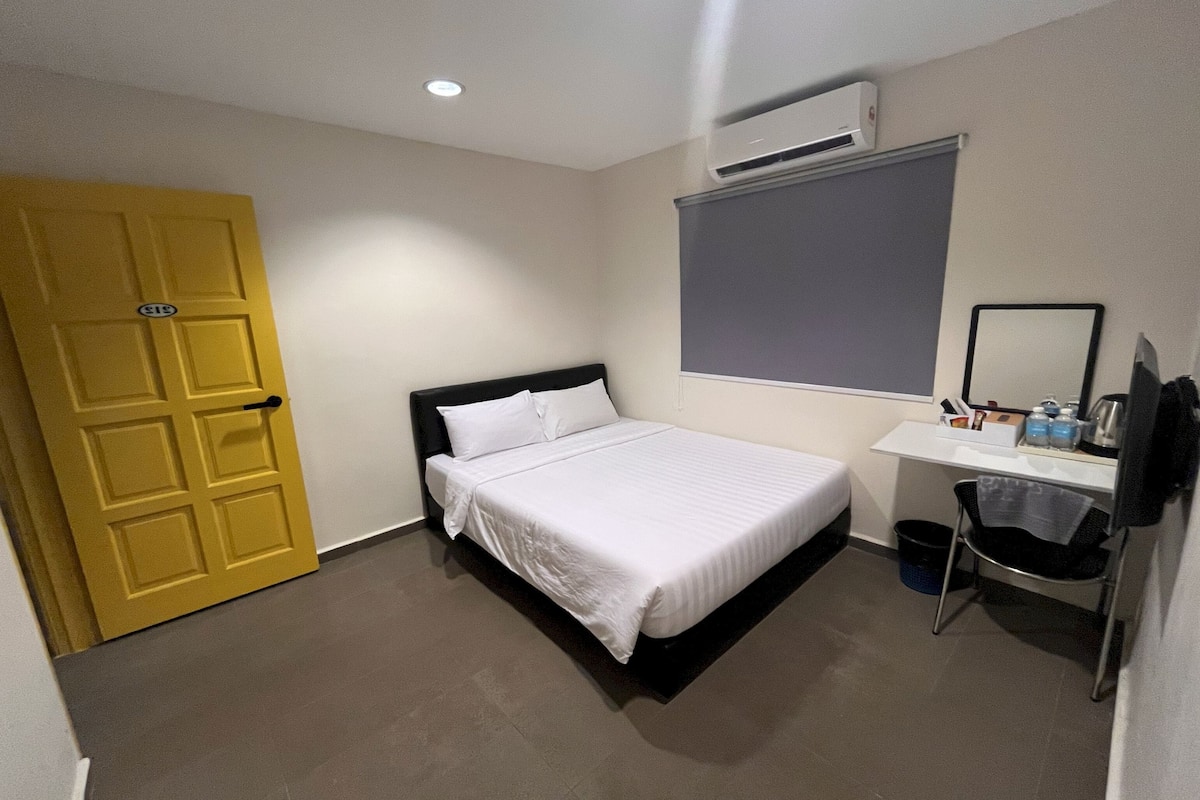 Una habitación de hotel con cama, escritorio, silla, puerta amarilla y equipo de aire acondicionado.