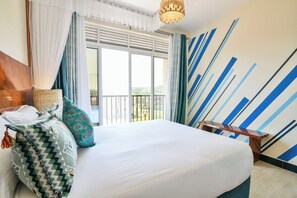 A hotel room with a large bed, a wooden headboard, a wicker basket, a patterned pillow, and a view of the outdoors through a balcony.