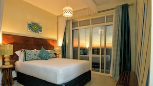A large bed with a wooden headboard, two bedside lamps, and decorative pillows. A sliding glass door leads to a balcony with a view of the sunset. - Hotel 256 Kampala (Kampala)