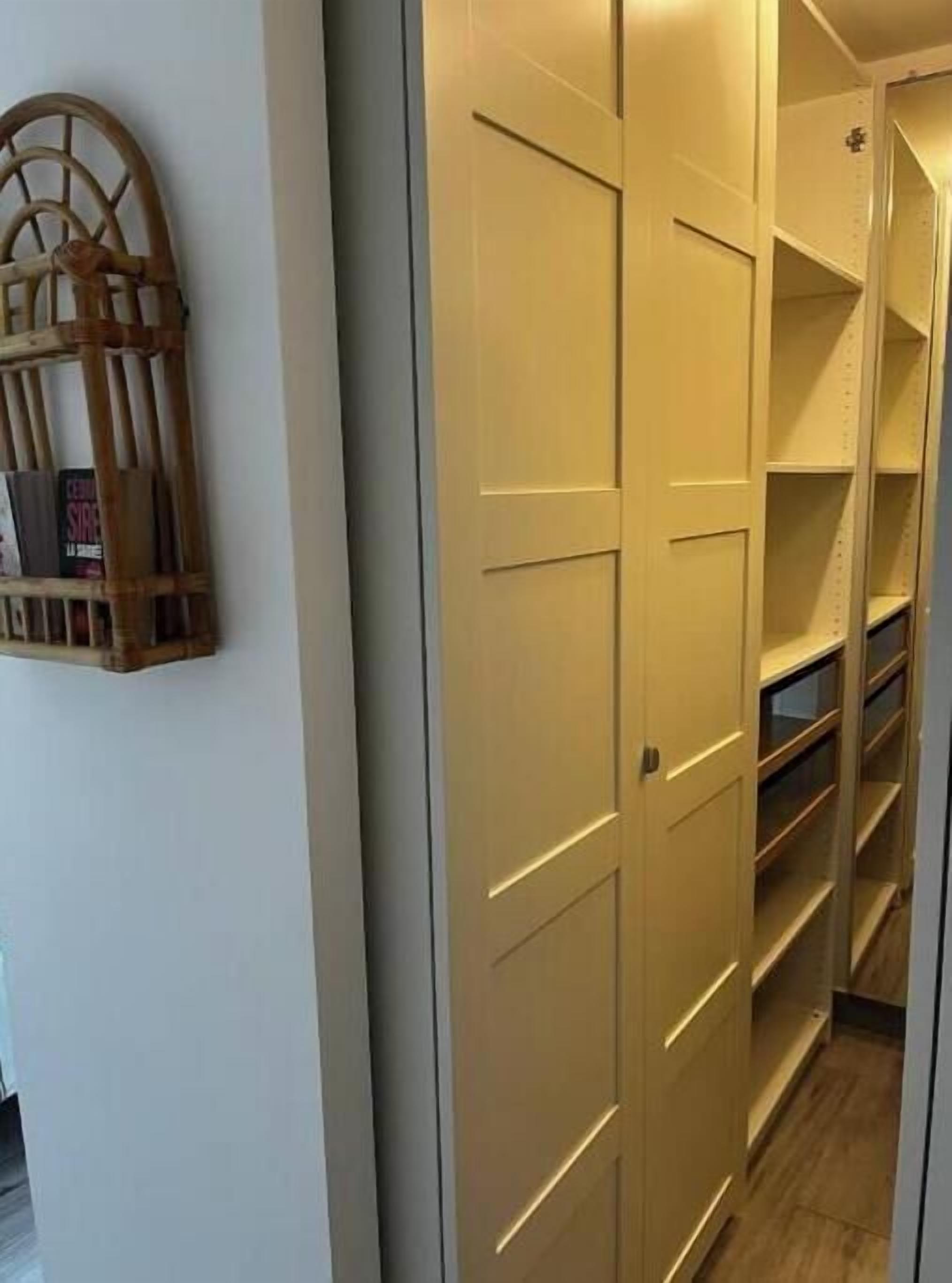 Een gang met een houten boekenkast, een beige garderobe met meerdere deuren en ingebouwde planken.