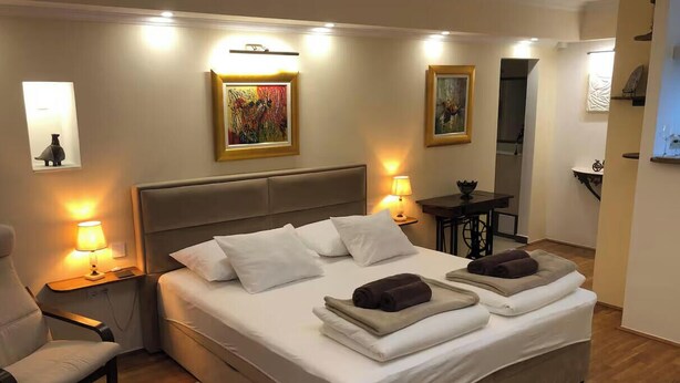 Une chambre d’hôtel avec un grand lit, des lampes de chevet, une chaise, une petite table et des œuvres d’art accrochées aux murs.