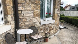 Un bâtiment en pierre avec une table ronde et deux chaises, une fenêtre ornée de fleurs rouges et une plante en pot.