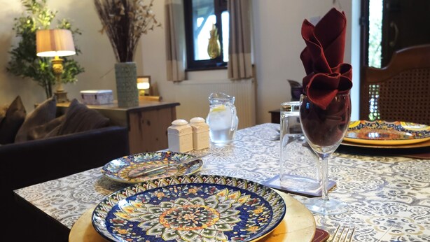A dining table with ornate plates, a glass of wine, and a vase with a red flower arrangement. - Langford Apartments and Rooms (Bristol)