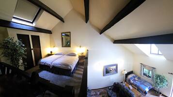 Una habitación con una cama grande, un sofá y una mesita. Hay una ventana con cortinas y una planta.